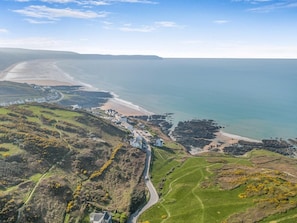 Un village côtier avec des maisons qui bordent une route sinueuse, une plage et une côte rocheuse.