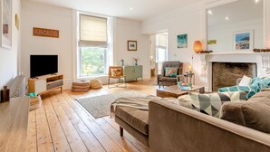 A spacious living room with a fireplace, a television, and a large window. - 3 Bed in Mortehoe (oc-pines) (Mortehoe)