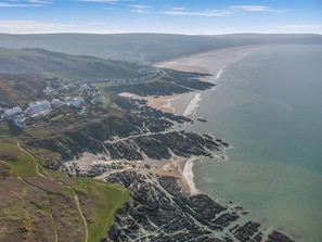 Vue aérienne d’une ville côtière avec une plage, une côte rocheuse et des bâtiments le long du rivage.