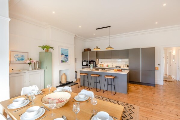 A modern kitchen with a central island, bar stools, and a dining area with a wooden table set for six.