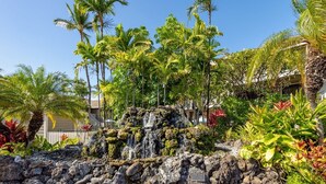 Un jardín tropical con una cascada, palmeras y un muro de piedra.