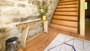 A rustic interior with a stone wall, wooden staircase, a bench, a rug, and a vase with flowers. - Hideaway Chalet Faazihaus in Ruhiger Panoramalage (Martisberg)