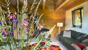 A cozy living room with a wooden ceiling, a green sofa, a colorful rug, and a vase of flowers. - Hideaway Chalet Faazihaus in Ruhiger Panoramalage (Martisberg)