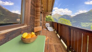 A wooden deck with a table and chairs, a bowl of fruit, and a scenic mountain view. - Hideaway Chalet Faazihaus in Ruhiger Panoramalage (Martisberg)