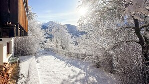 A snow-covered pathway flanked by buildings and trees, leading to a mountainous backdrop. - Hideaway Chalet Faazihaus in Ruhiger Panoramalage (Martisberg)
