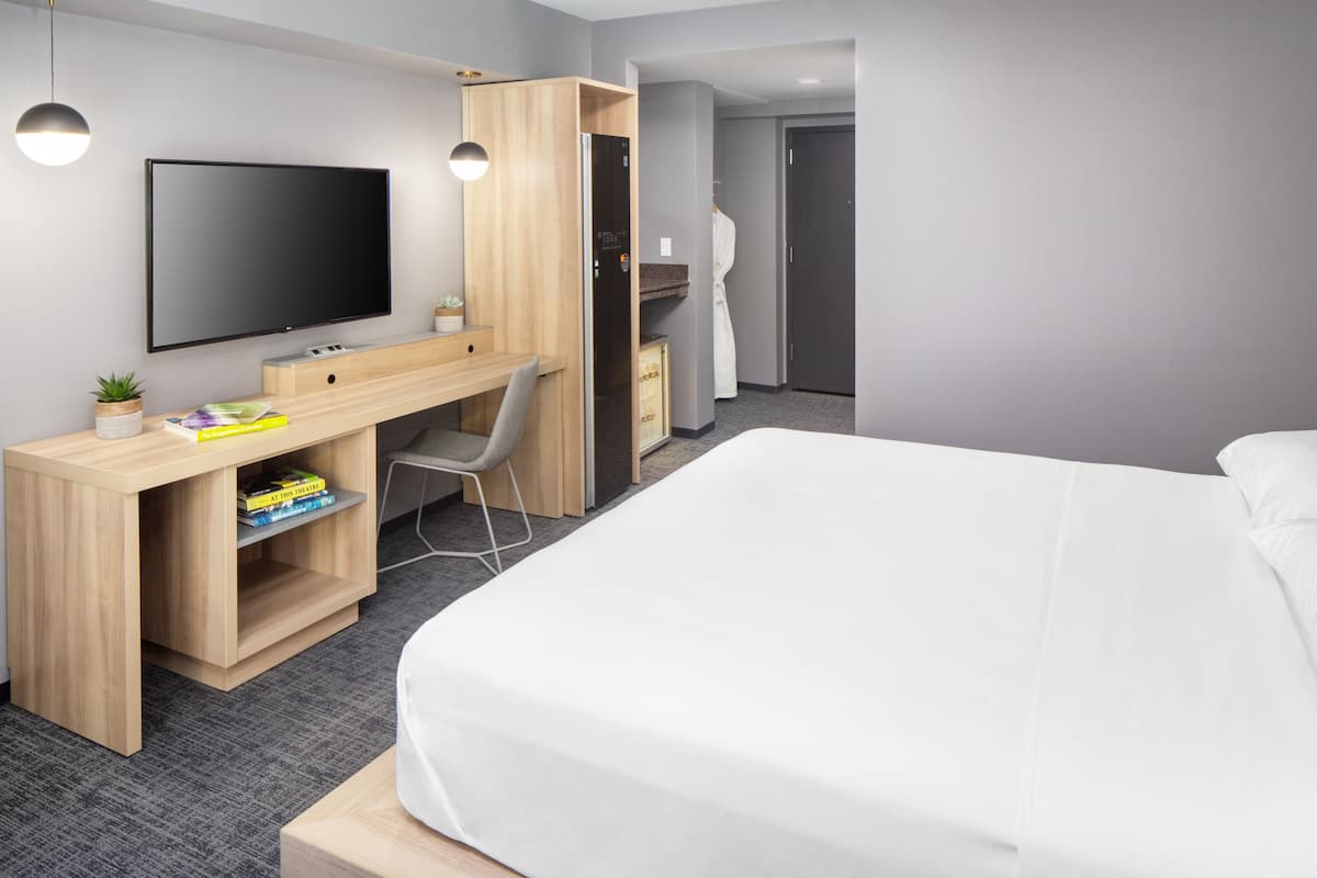 Une chambre d’hôtel moderne dotée d’un grand lit, d’un bureau en bois avec une chaise, d’une télévision à écran plat et d’une armoire.