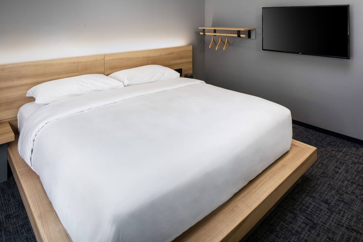 Un lit bien fait, avec une tête de lit en bois, un téléviseur à écran plat fixé au mur et une simple table de chevet.
