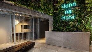 Un espace d’accueil moderne, avec un panneau lumineux au néon, un comptoir d’accueil, un banc en bois et un mur végétal.