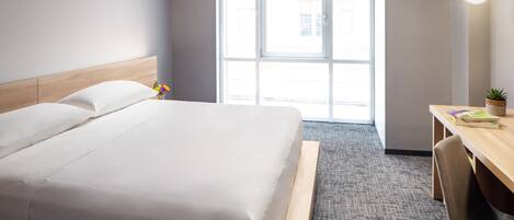 Habitación de hotel con cama, escritorio, silla, ventana y una planta.