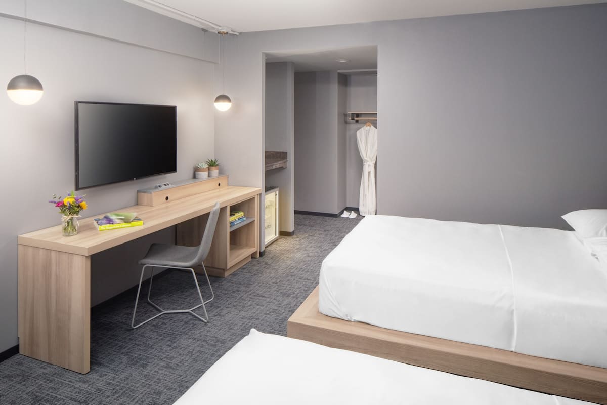 Une chambre d’hôtel moderne dotée d’un grand lit, d’un bureau avec une chaise, d’une télévision à écran plat et d’une douche à l’italienne.