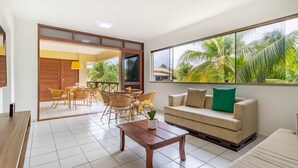 A modern living room with a sofa, coffee table, and dining area with chairs and a table. - GB22 Ótimo Apt 3 Quartos - Guarajuba (Camaçari)