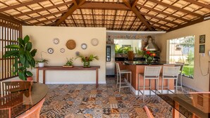 A kitchen with a tiled floor, a wooden ceiling, and a bar area with chairs. - GB22 Ótimo Apt 3 Quartos - Guarajuba (Camaçari)