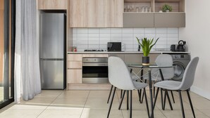 Eine moderne Küche mit Edelstahlkühlschrank, integriertem Backofen und einem Essbereich mit grauen Stühlen und einem Glastisch.