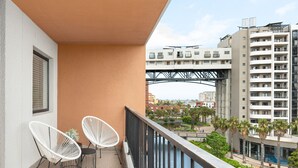Ein Balkon mit zwei weißen Stühlen und einem kleinen Tisch, mit Blick auf einen Fluss und eine Brücke.