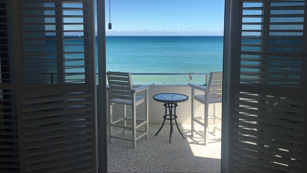 A balcony with a view of the ocean, a table, two chairs, and a hanging light fixture. - Best Studio Location In The Building With Unobstructed Water View Balcony (Fort Lauderdale)