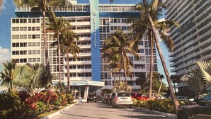A hotel with a central blue sign, multiple floors, and palm trees. - Best Studio Location In The Building With Unobstructed Water View Balcony (Fort Lauderdale)