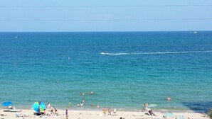 A beach with people swimming and sunbathing, a boat in the water, and a clear sky. - Best Studio Location In The Building With Unobstructed Water View Balcony (Fort Lauderdale)