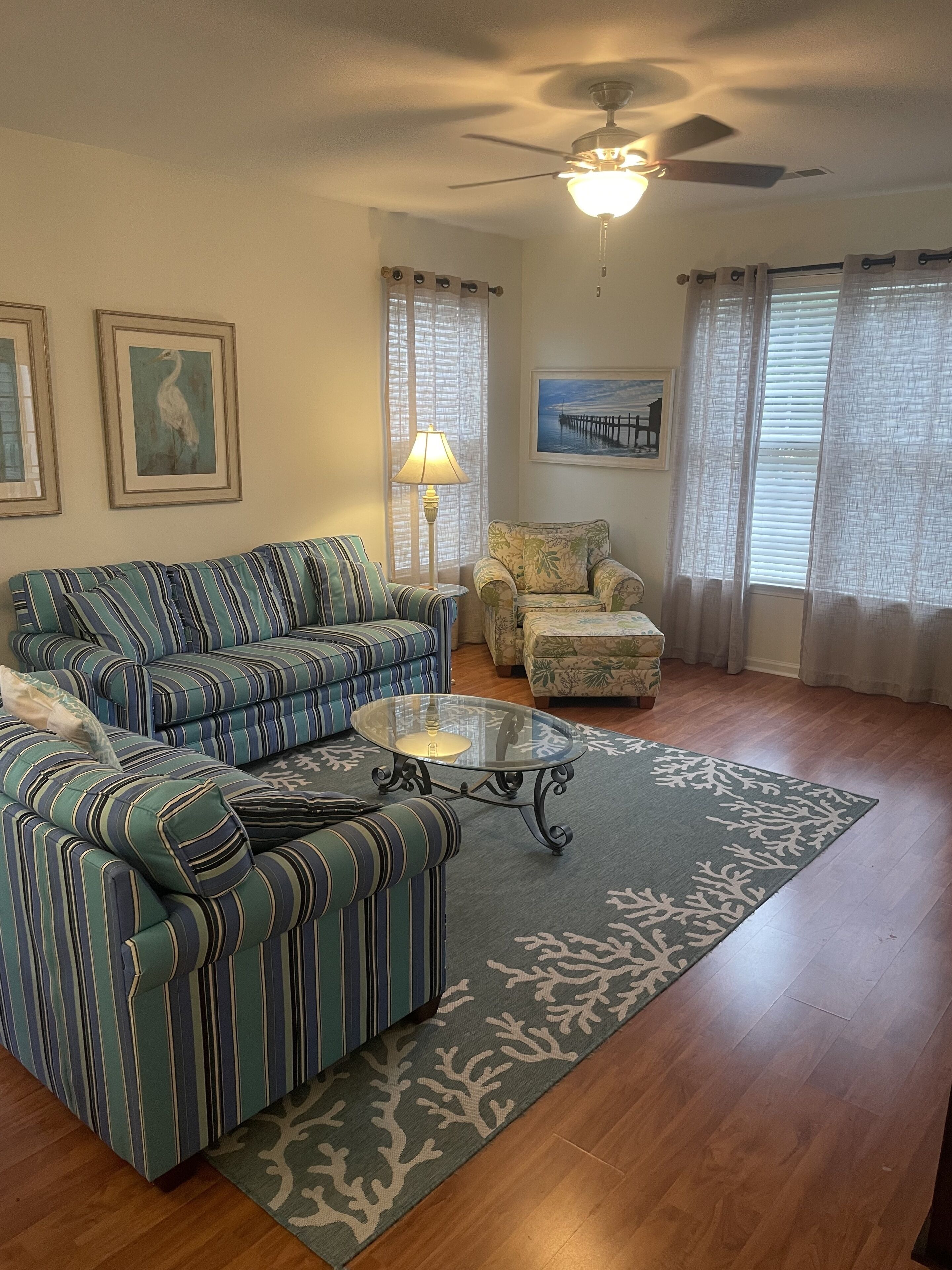 A living room with a striped sofa, a round coffee table, a patterned armchair, and a ceiling fan.