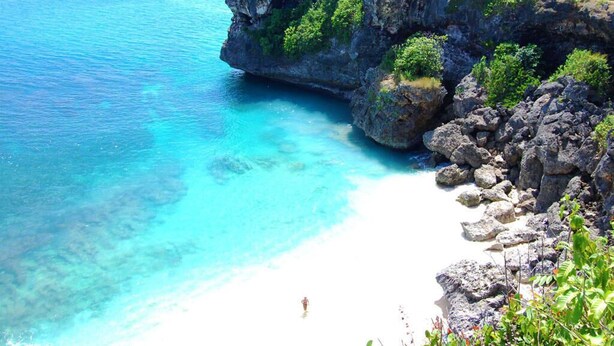 Un paisaje costero con mar azul cristalino, acantilados rocosos y una playa arenosa.