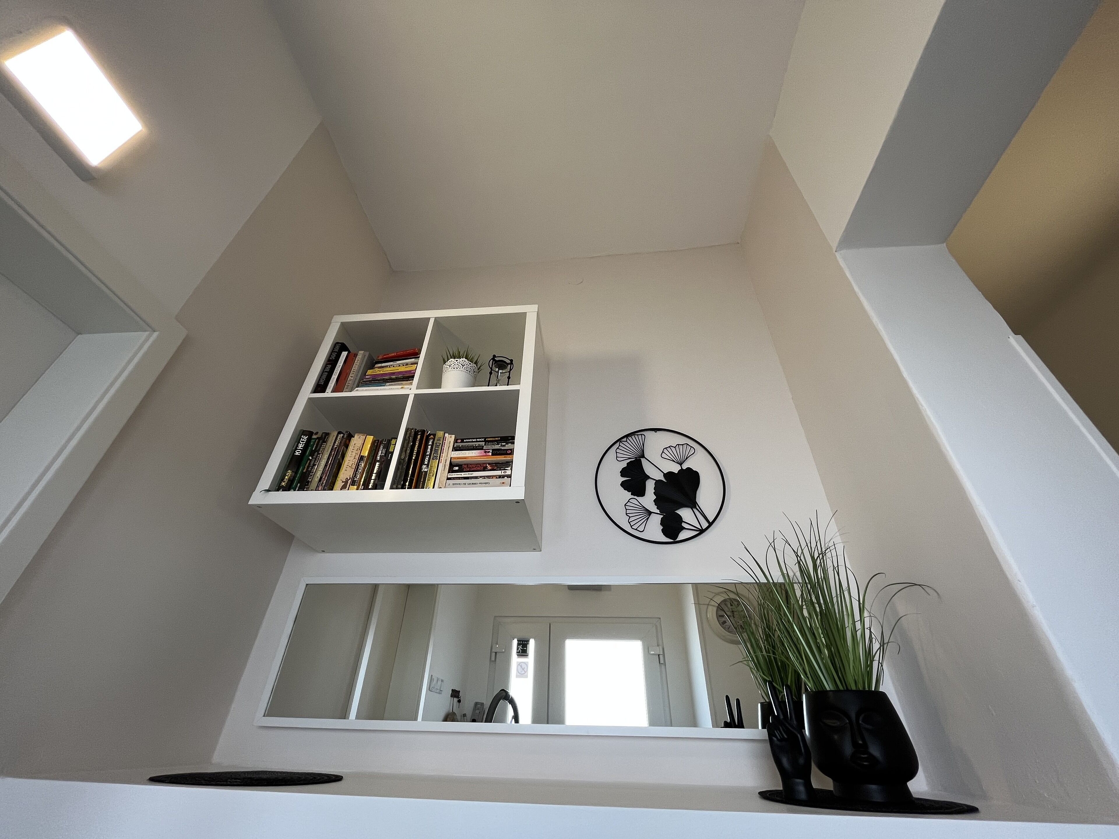 Ein Zimmer mit einem weißen Bücherregal, einem runden Kunstwerk an der Wand und einer Topfpflanze.