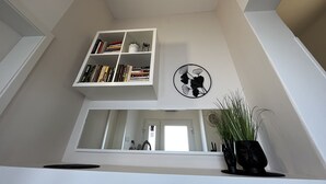 Una habitació amb una estanteria blanca, una obra d'art circular penjada a la paret i una planta en test.