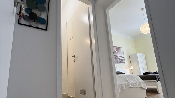 Passadís que condueix a una habitació amb un llit, una porta i una obra d'art penjada a la paret.
