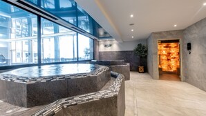 Un área de spa moderna con un amplio jacuzzi, una pared de vidrio y una pared de piedra con iluminación cálida.