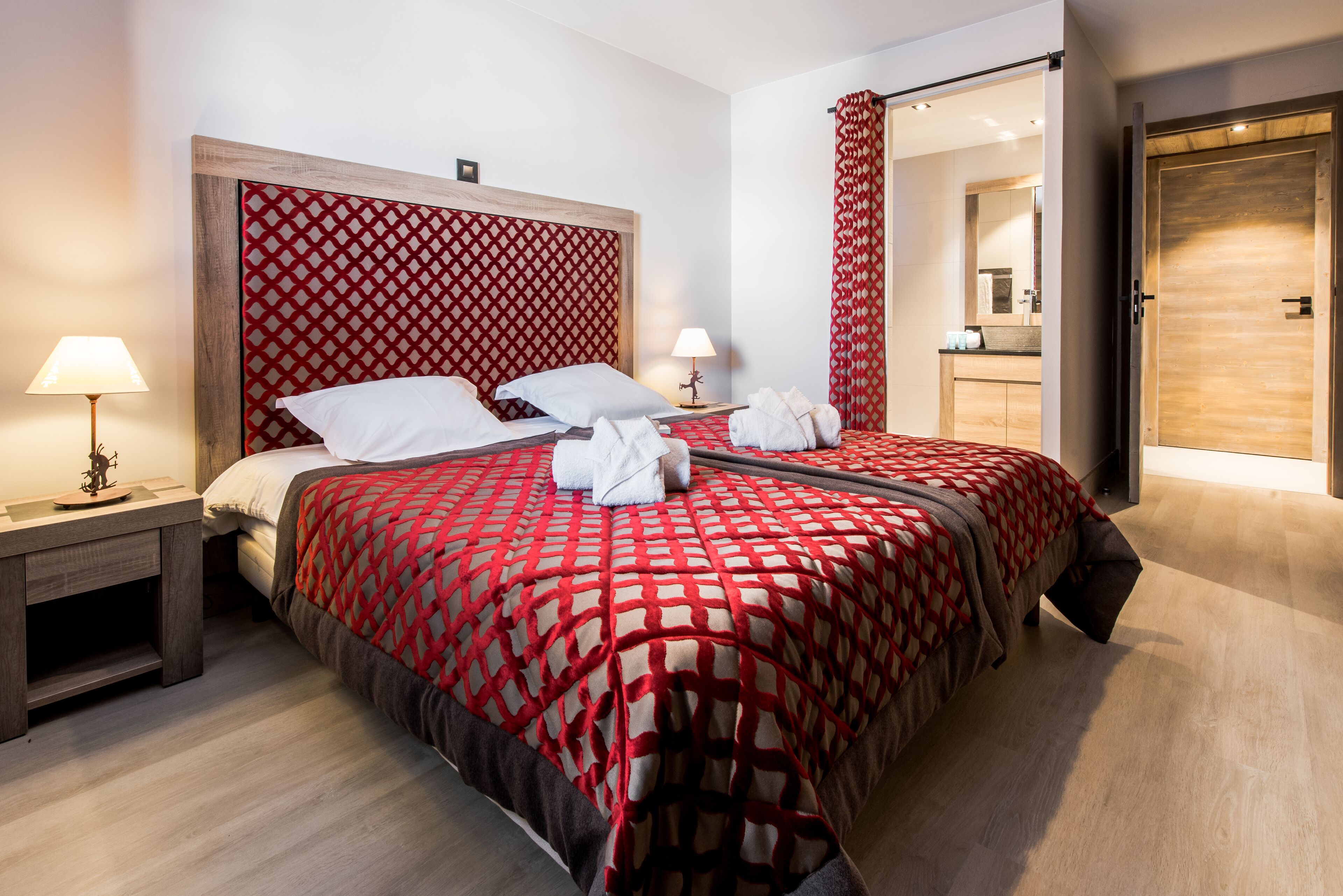 Ein ordentlich bezogenes Bett mit einer rot-weißen Karodecke, zwei Nachttischlampen und einem hölzernen Kopfteil.