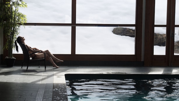 Una persona descansando junto a una ventana con vista a una piscina.