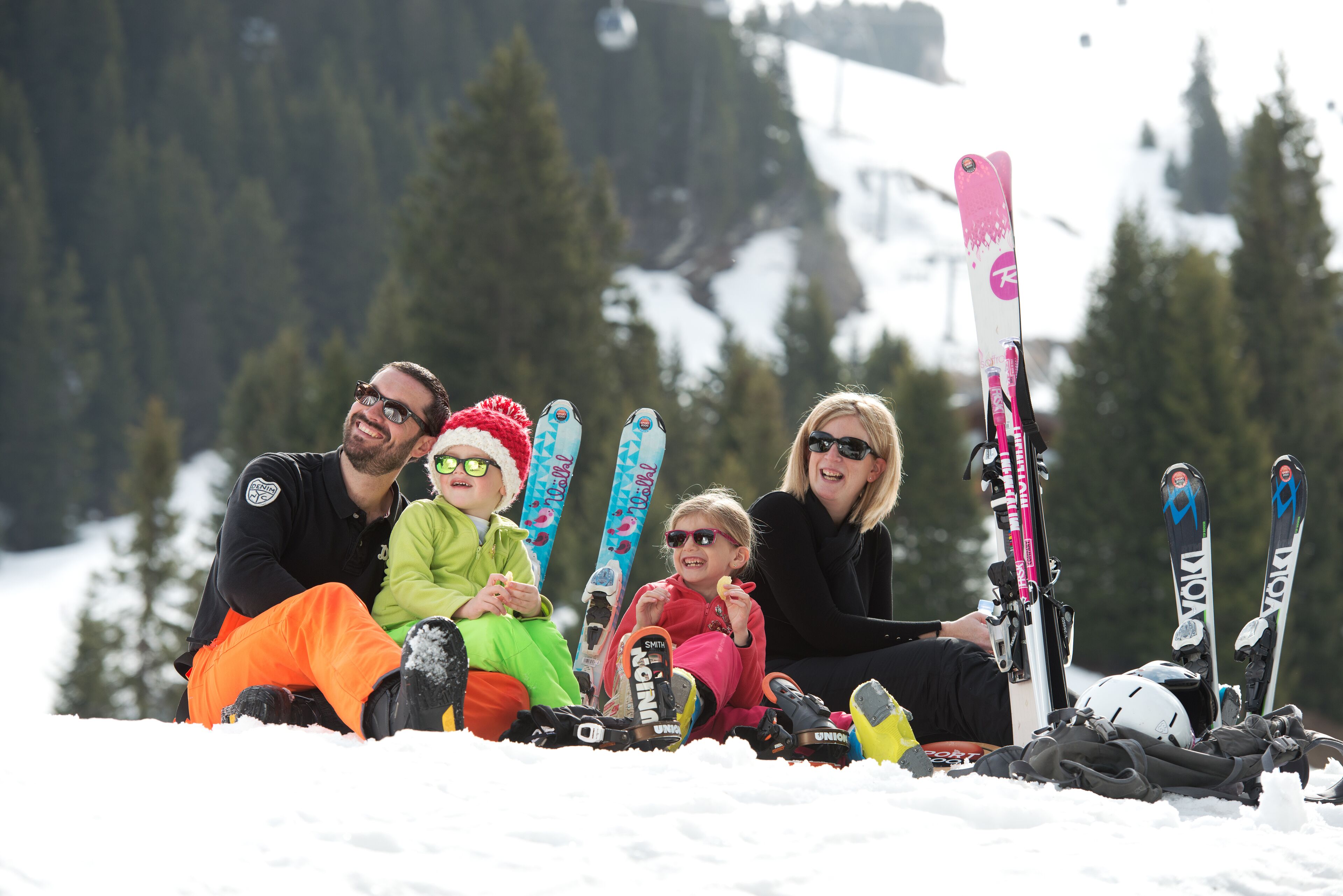 A group of people sitting on the snow with skis and ski poles around them.