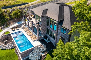 A modern house with a swimming pool, stone exterior, and large windows. - MAIN CHANNEL views, private pool, hot tub, man cave, and game room! Sleeps 30! (Osage Beach)