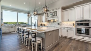 A spacious kitchen with a large island, white cabinetry, and a stone backsplash.