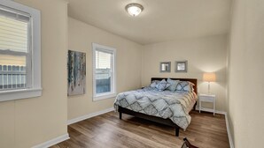 Ein Schlafzimmer mit einem Bett, zwei Fenstern, einem Nachttisch, einer Lampe und einer Deckenleuchte.