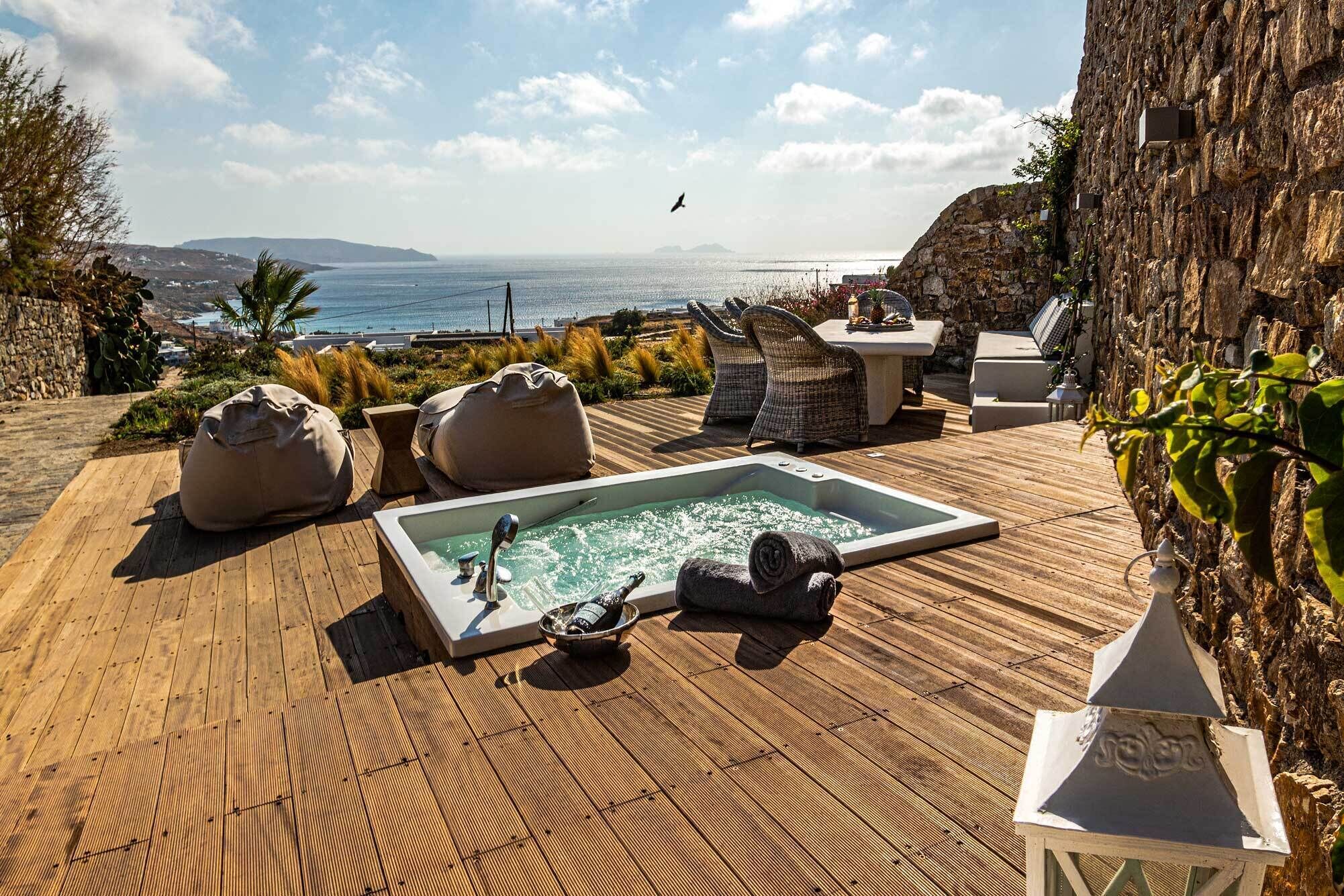 Una terraza de madera con un jacuzzi, sillones de descanso y vistas al mar.