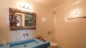 A bathroom with a blue sink, a rustic mirror, and a toilet. - Kallisti (Mykonos)