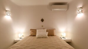 A neatly made bed with a patterned bedspread, two bedside lamps, and an air conditioning unit above the bed. - Kallisti (Mykonos)