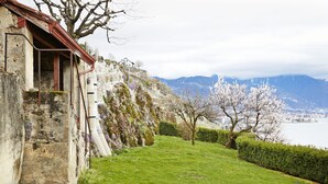 Un bâtiment en pierre avec un toit rouge, un chemin pavé et une zone herbeuse avec des arbres.