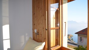 Une pièce de cabane en bois comprenant un lit, une fenêtre donnant sur les montagnes et un lac, ainsi qu’un banc en bois.
