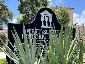 A sign for West Settlers Historic Town with palm trees and a building in the background.