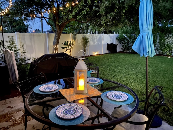 A round glass table with four blue and white patterned plates, a lit lantern, and a blue umbrella.