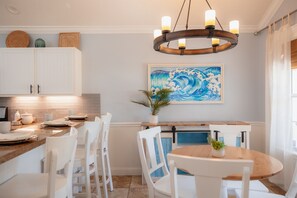 A kitchen with white cabinets, a wooden dining table, and a hanging light fixture. - Private Beach Bar Vibes | Pool, Grill + Games (Jacksonville Beach)