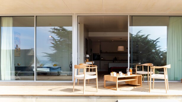 A modern interior with a glass door leading to a balcony, wooden furniture, and a kitchen area.