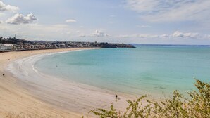 A coastal beach with a sandy shore, a clear blue sea, and a town in the background.