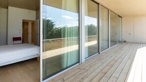 A modern room with a wooden floor, a bed, and large sliding glass doors leading to an outdoor area.