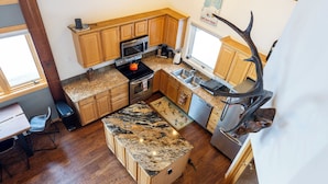 A modern kitchen with wooden cabinets, granite countertops, and a built-in oven. - 100 Steps Away, Ski in Ski Out Condo (Big Sky)