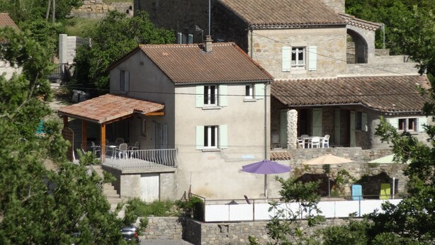 Ein Gebäude aus Stein mit einem Ziegeldach, einem Balkon und einer kleinen Sitzgelegenheit im Freien mit Sonnenschirmen.