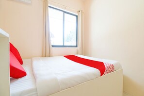 A single bed with white bedding and red accents, a window with curtains, and a white wall. - J5 Guest House & Restobar (Moalboal)