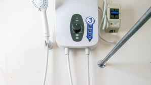 En vit duschkabin från Voda med ett handhållet duschmunstycke, ansluten till en väggmonterad kontrollpanel med en strömbrytare och en digital display.