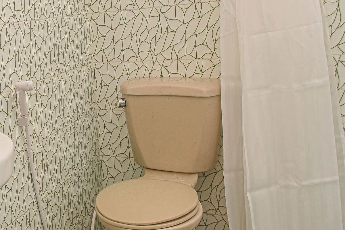 A bathroom with a toilet, a shower curtain, and patterned wallpaper.
