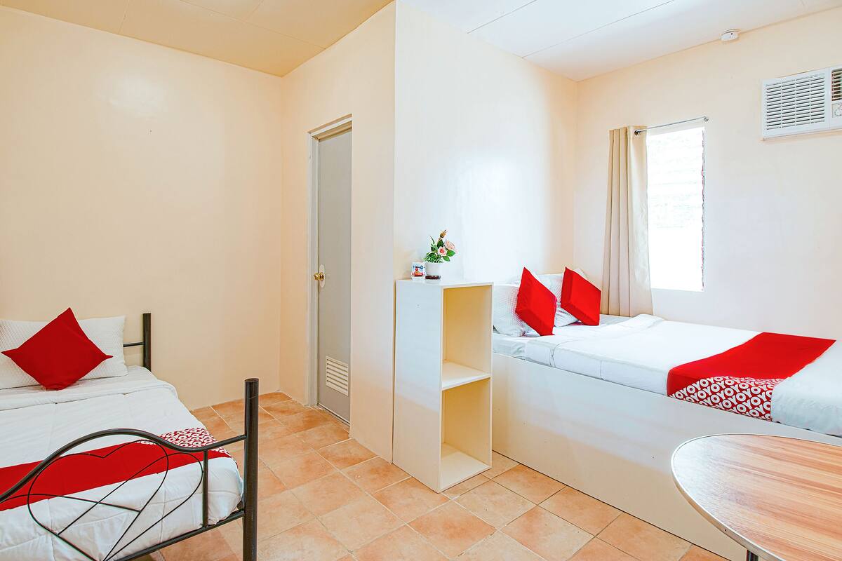 Une chambre avec deux lits, une petite table et une porte donnant sur une autre pièce.